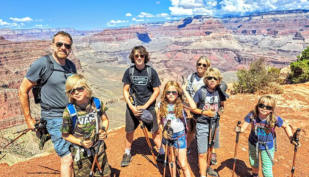 A group of six individuals appearing to be a family is posing with hiking sticks against the backdrop of the Grand Canyon under a clear blue sky