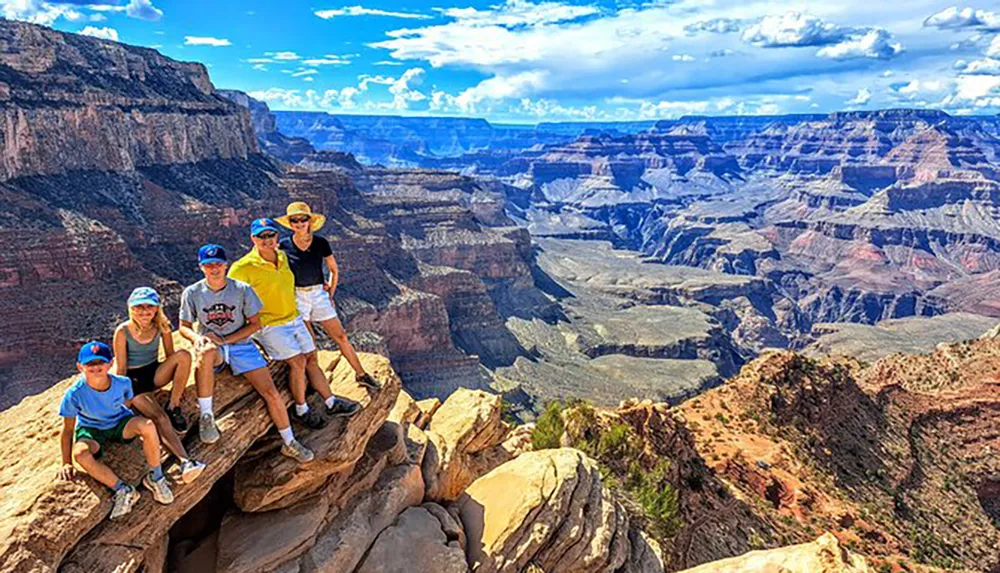 A group of people are posing for a photo on a rocky outcrop with the expansive view of the Grand Canyon in the background
