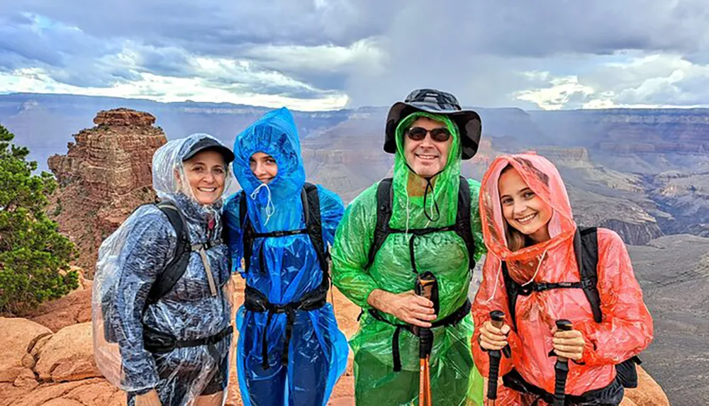 Four smiling hikers wearing colorful rain ponchos are standing in front of a scenic canyon vista