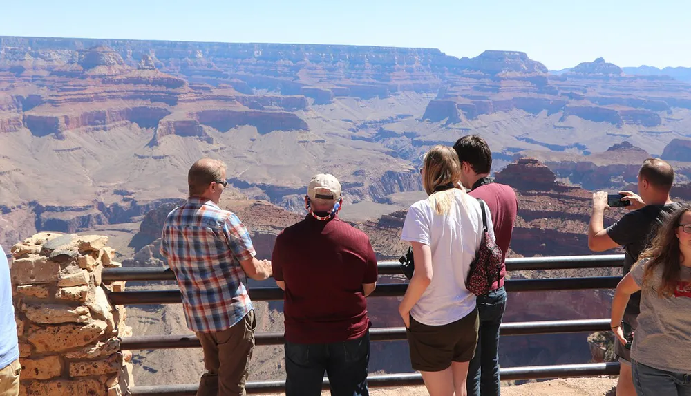 Tourists are enjoying the view of the Grand Canyon from a lookout point on a sunny day