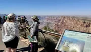Tourists admire the expansive view of the Grand Canyon from a viewing platform with informational signage.