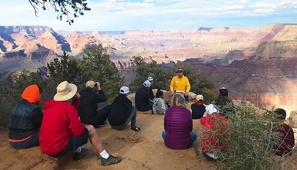 A group of people listens to a speaker against the backdrop of the Grand Canyon