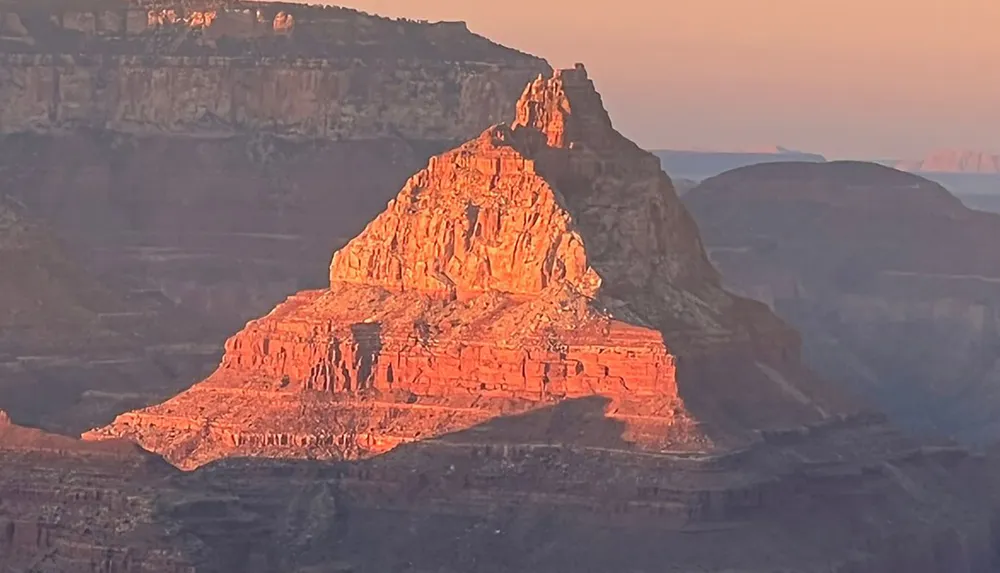 The image captures a glowing red rock formation under the subtle light of sunset at the Grand Canyon