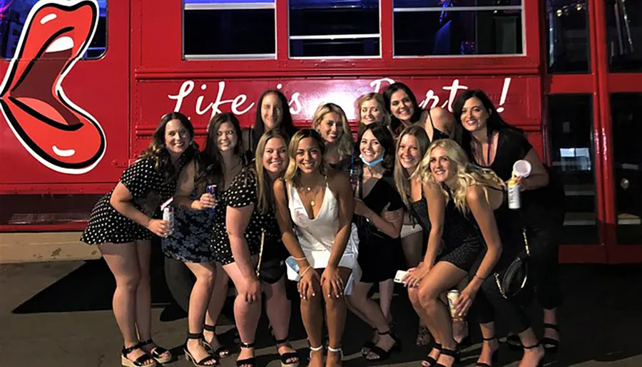 A group of people is posing for a photo in front of a red double-decker bus with a large tongue logo and the phrase Life is short.