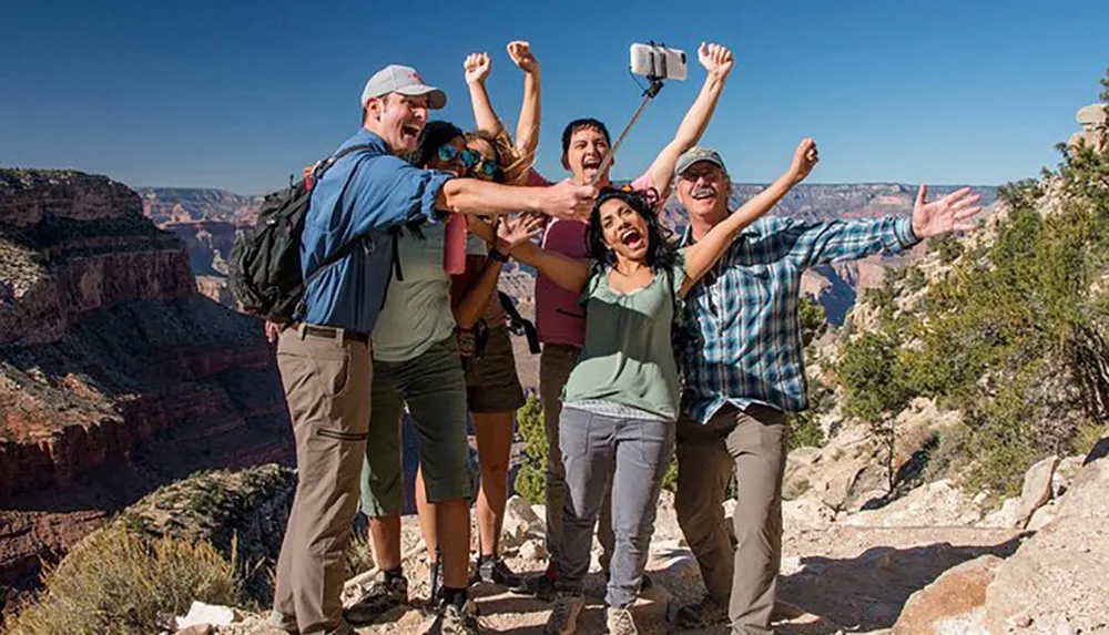 A group of happy hikers is taking a selfie at the edge of a canyon under a clear blue sky
