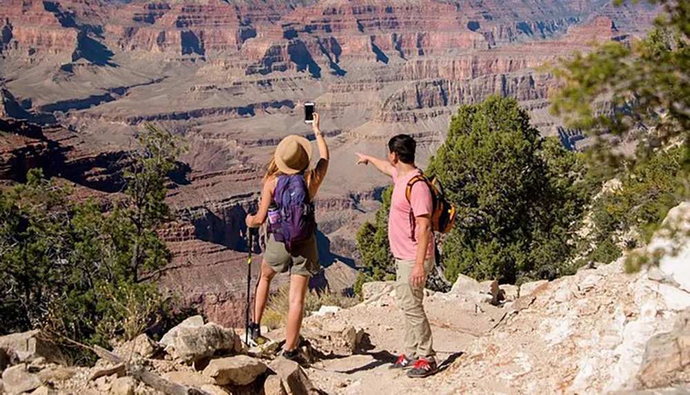 Two hikers are capturing a selfie with the picturesque backdrop of the Grand Canyon