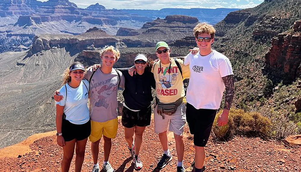 Five people are posing for a photo with the scenic Grand Canyon in the background on a sunny day