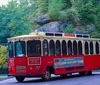 A red and white trolley labeled Wisconsin Dells City and History Tour is traveling on a road next to rock formations and lush trees