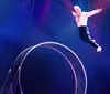 A performer is standing onstage with mechanical wings extended while two assistants appear to be adjusting the base of the wings amidst colorful stage lighting