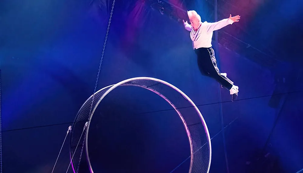 A performer is walking on a spinning wheel high above the ground in what appears to be a circus or acrobatic act