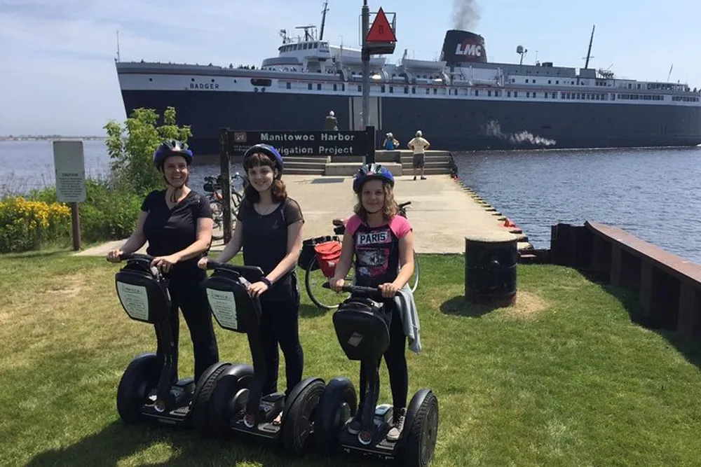 Three people are posing with Segways in front of a large ship anchored in a harbor