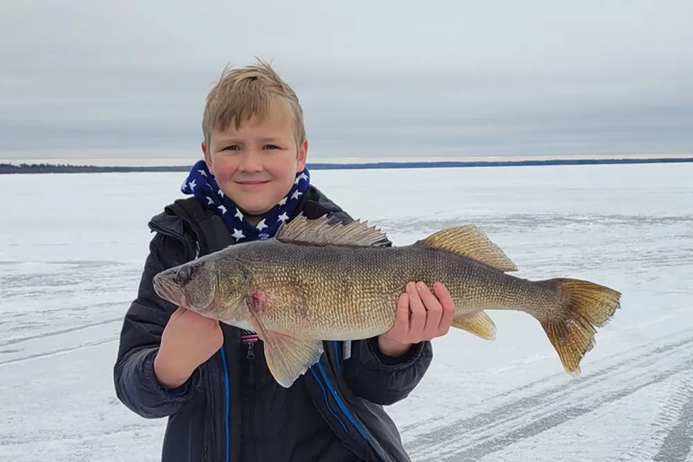 A young boy is holding a large fish with pride on a frozen lake surface