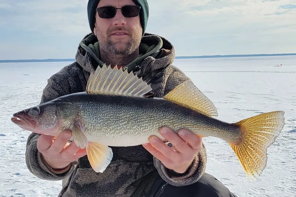 A person is holding a large fish with a snowy landscape and ice in the background indicating ice fishing success