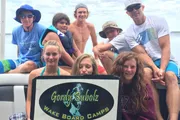 A group of people, likely from a wakeboarding camp, are posing for a photo with a sign that says 