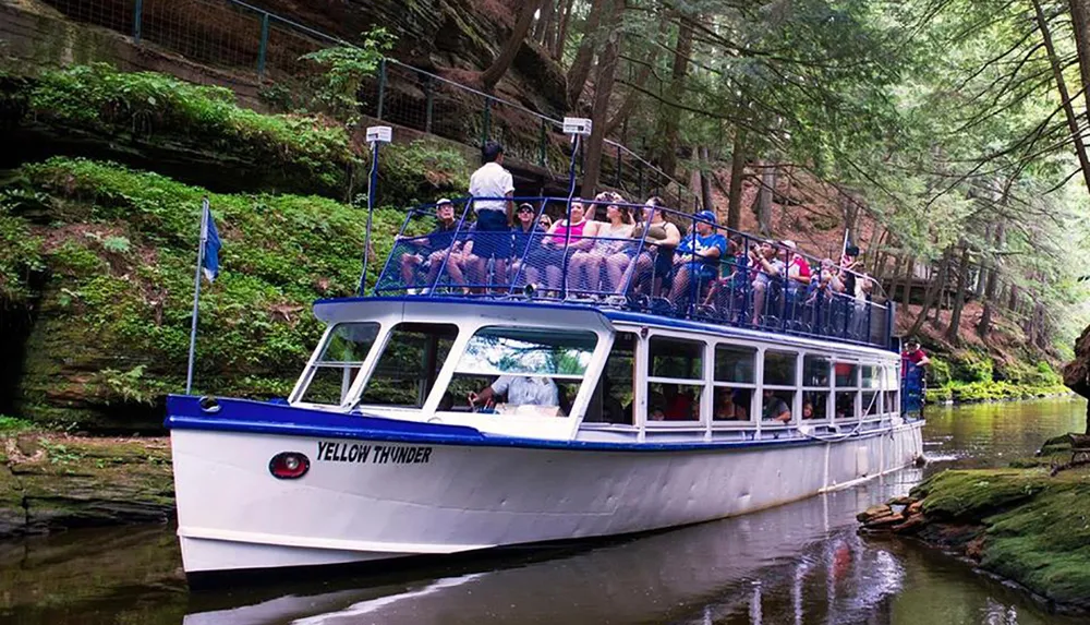 A boat named YELLOW THUNDER is carrying a group of passengers through a scenic waterway surrounded by lush forests and rock formations