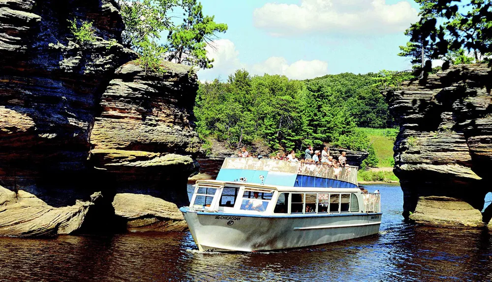 A tour boat named Chicagow is navigating between two large rock formations carrying passengers exploring a scenic waterway