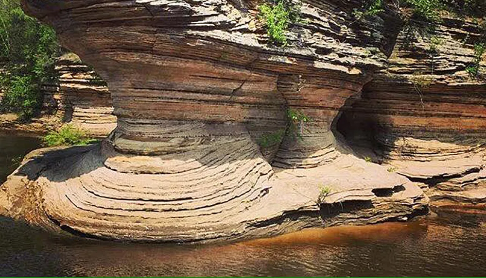 The image shows a large rock formation with distinctive layered strata and a natural arch over a body of water