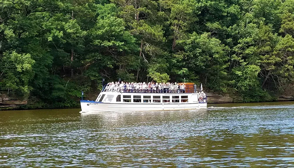 A group of passengers is aboard a river cruise boat enjoying a scenic tour along a tree-lined waterway