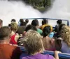 A group of people are enjoying a ride on a blue jet boat named HAWK on a sunny day with natural rock formations in the background