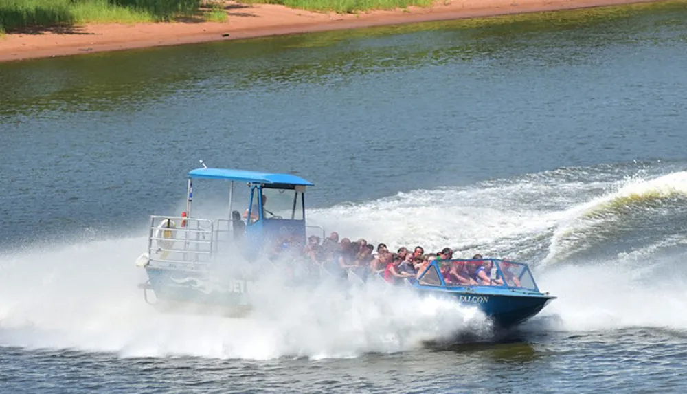 A group of people appear to enjoy a high-speed jet boat ride creating a large spray of water as they move across the river