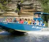 A group of people are enjoying a ride on a blue jet boat named HAWK on a sunny day with natural rock formations in the background