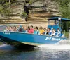 A group of people are enjoying a ride on a blue jet boat named HAWK on a sunny day with natural rock formations in the background