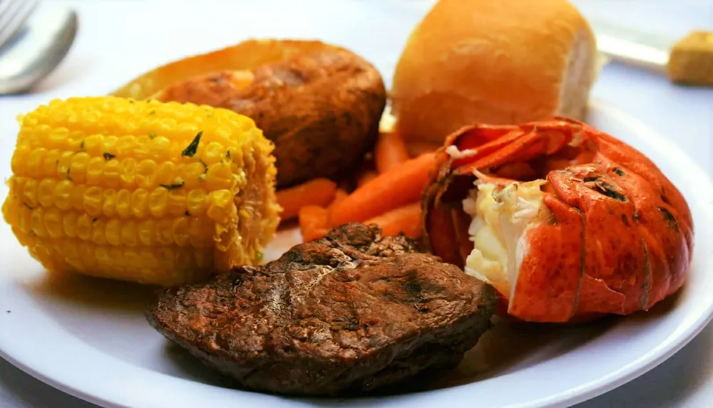 The image showcases a plated surf and turf meal with steak lobster corn on the cob carrots and a baked potato