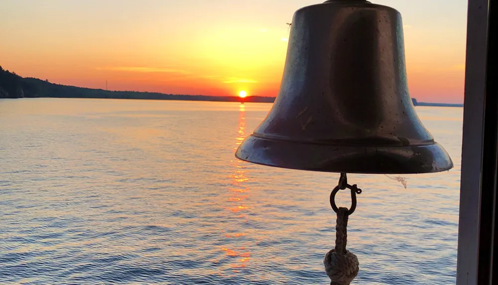A ships bell is silhouetted against a stunning sunset over the tranquil sea