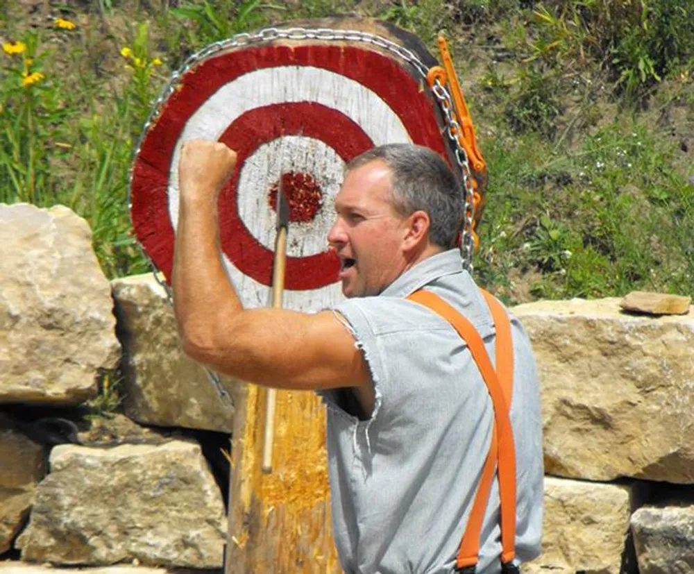 A man is lifting a traditional alpine log with a target painted on it possibly during a folk festival or competition