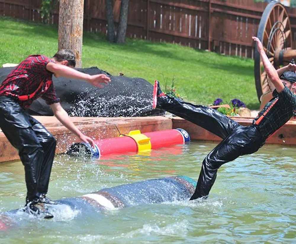 Three people are involved in a playful water activity where one is tipping over into the water while another watches and the third is partially submerged creating a dynamic and humorous scene