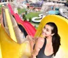 A person is sitting at the top of a water slide smiling back at the camera with a water park in the background