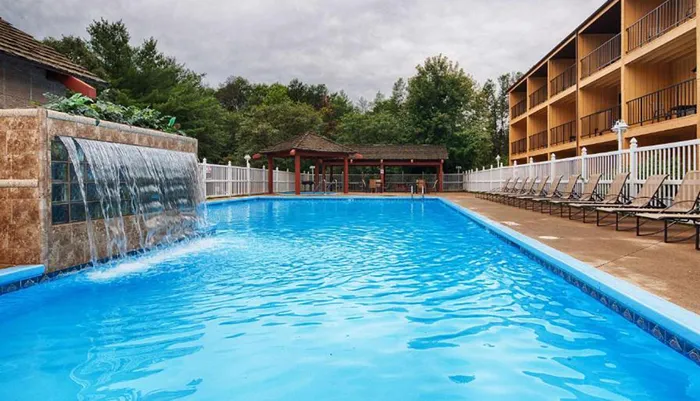 The image shows an outdoor swimming pool with a waterfall feature surrounded by lounge chairs and a building with multiple balconies