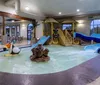 The image shows an indoor water park with a playful design featuring a pelican statue a small water slide and a childrens play structure