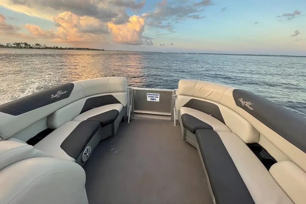 The image shows the interior of a pontoon boat with comfortable seating positioned on calm waters under a sky with scattered clouds during what appears to be early evening