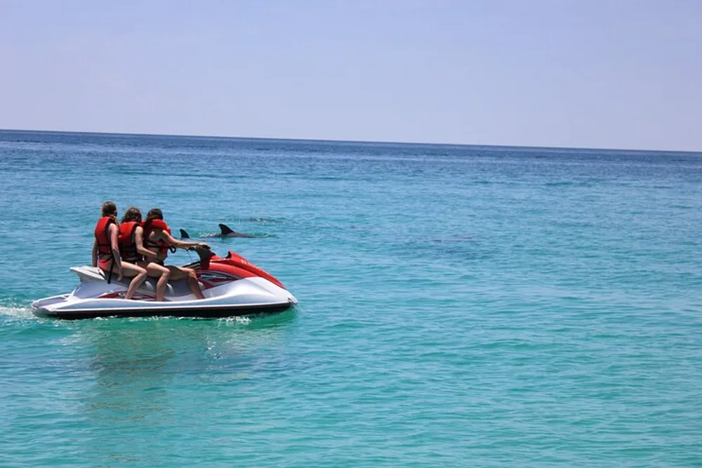 Three people in life jackets are riding a jet ski on a clear turquoise sea