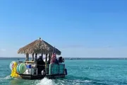 A tiki bar-themed boat carrying people is cruising on clear blue waters.