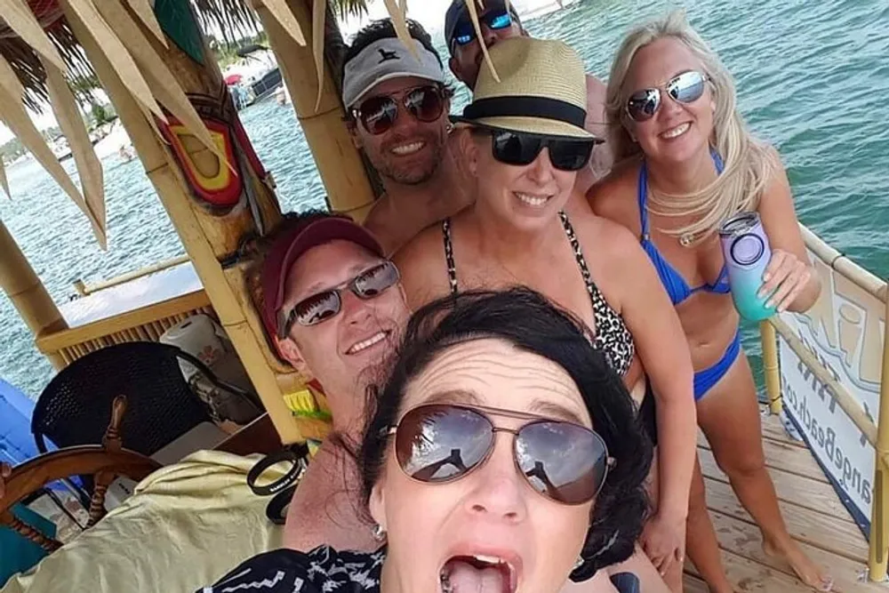A group of five smiling people are taking a selfie together on a tropical-themed boat bar