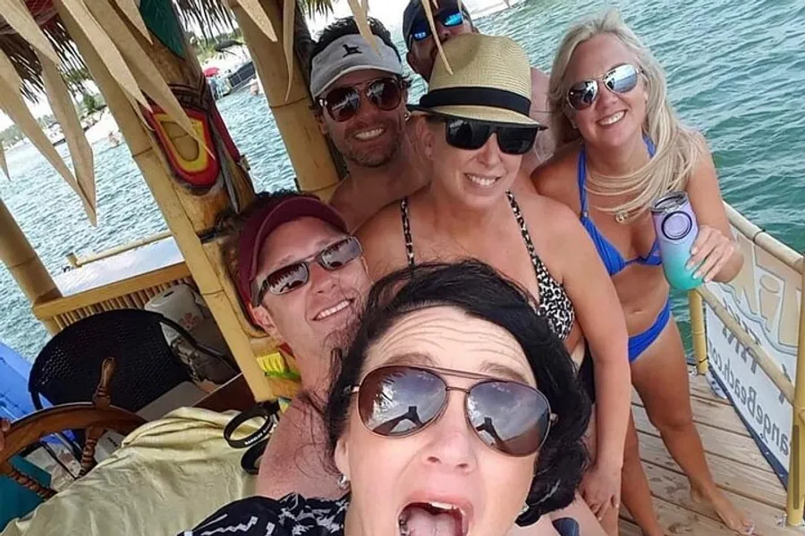 A group of five smiling people are taking a selfie together on a tropical-themed boat bar.