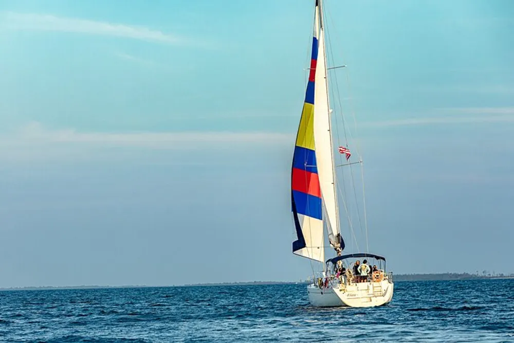 A sailboat with a colorful sail glides through the blue waters with people on board enjoying the ride