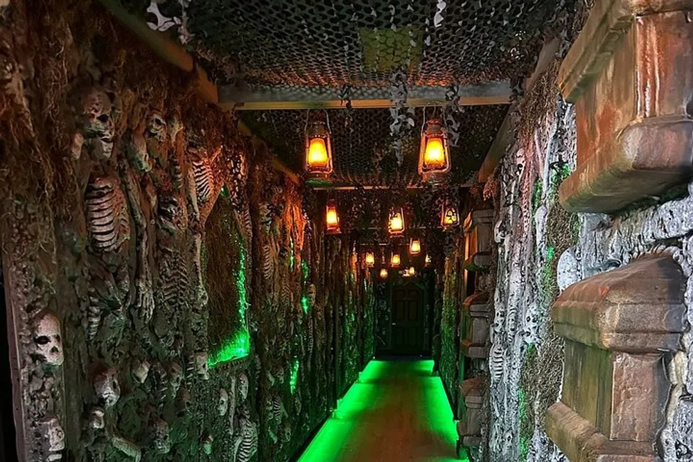 This image shows a corridor styled with a horror theme featuring walls adorned with skeleton bones and skulls green lighting on the floor and a gothic atmosphere intensified by hanging chains and dimly lit lanterns
