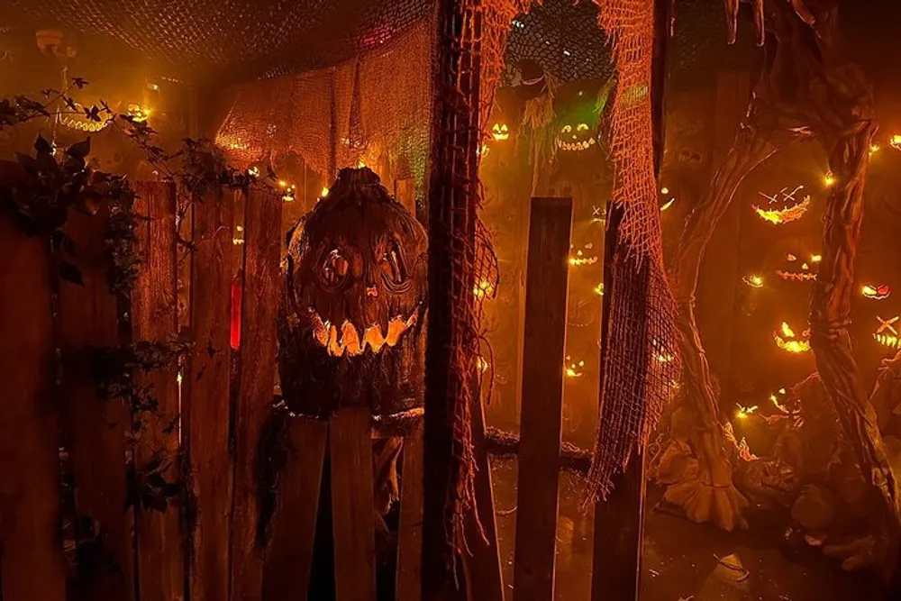 The image displays a Halloween-themed setting with menacing carved pumpkins illuminated in an eerie orange light amidst cobwebs and rustic wooden fencing