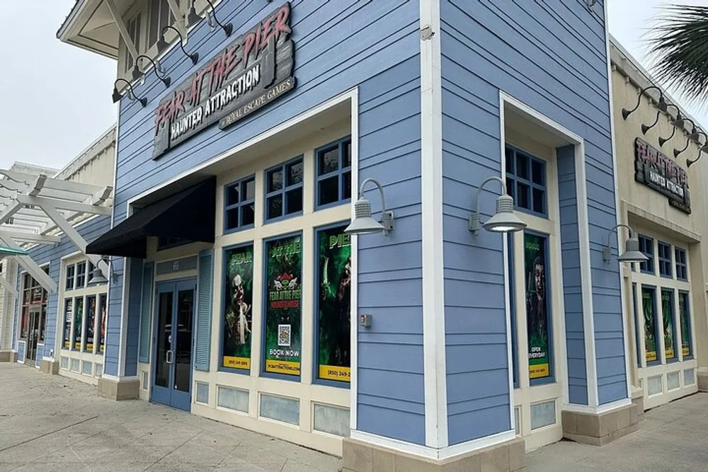The image shows a blue building adorned with signage for a haunted attraction called Pirate Pier featuring posters for what appears to be a spooky experience with a somewhat overcast sky above