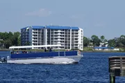 A blue and white tour boat is cruising along a waterway with a multistory building in the background under a clear blue sky.