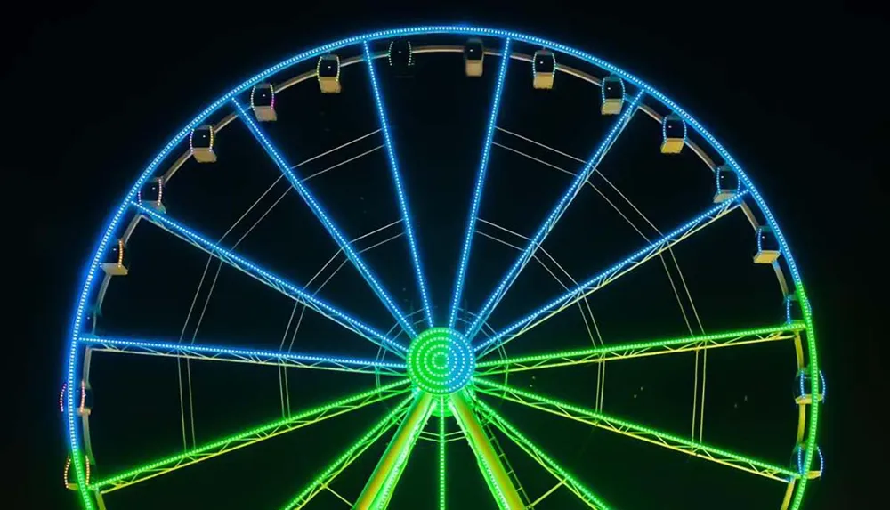 The image shows a brightly lit Ferris wheel at night featuring vivid blue and green neon lights that outline its structure and gondolas