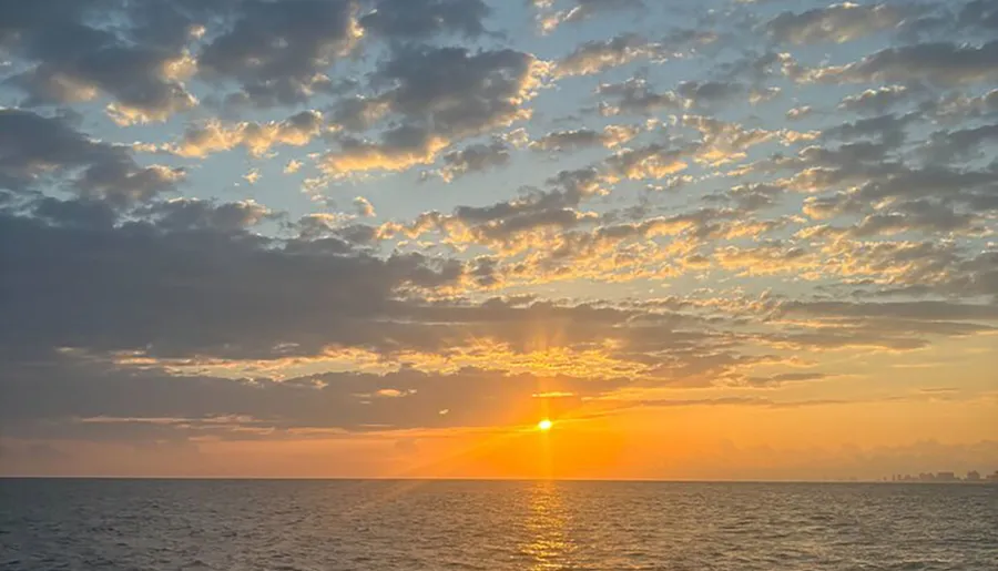 A serene sunset view over the ocean with scattered clouds reflecting the warm sunlight.