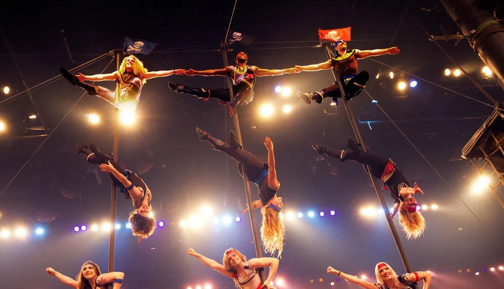 A group of acrobats perform an impressive aerial stunt on poles surrounded by bright stage lights