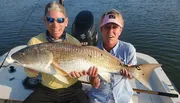 Two people on a boat proudly display a large fish they have caught.