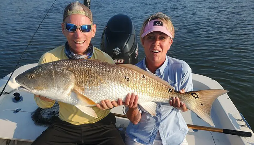 Two people on a boat proudly display a large fish they have caught