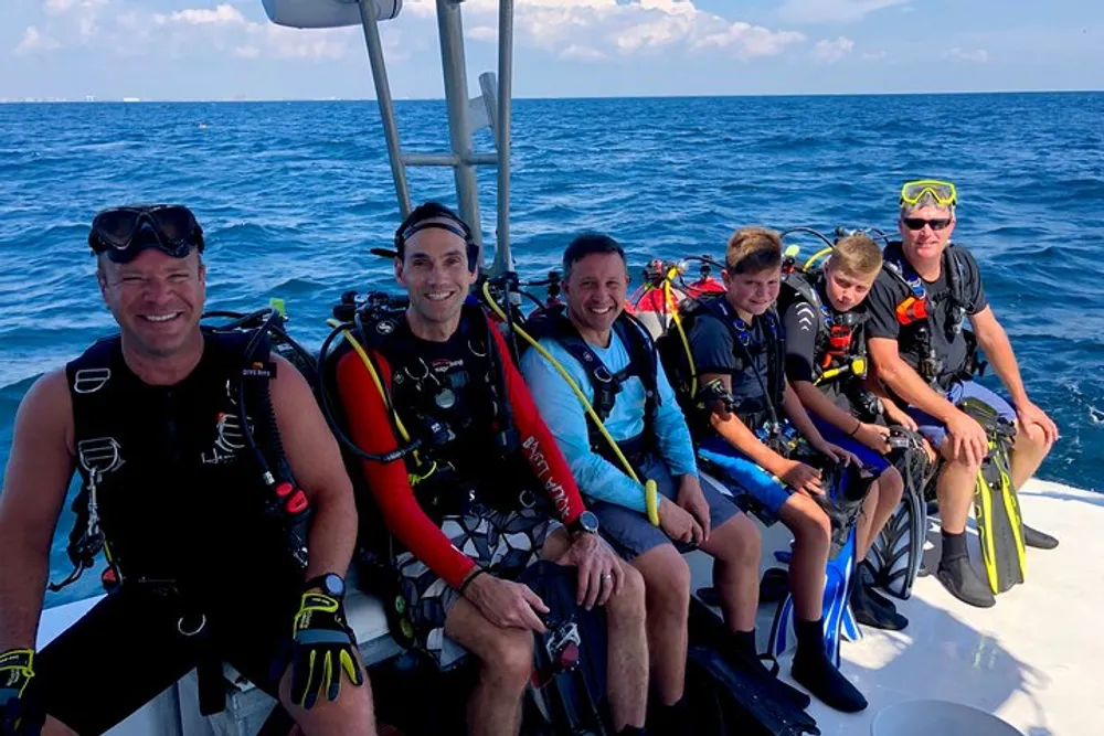 A group of six divers equipped with scuba gear are seated on the edge of a boat ready for a dive in the ocean