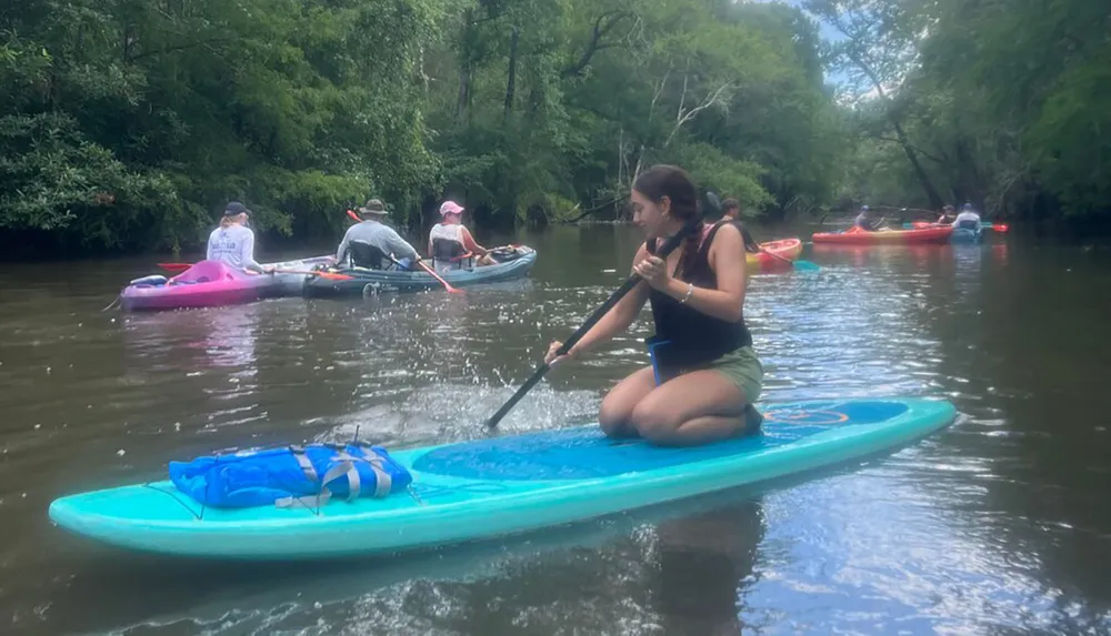 A group of people are leisurely paddleboarding and kayaking down a calm river flanked by lush greenery